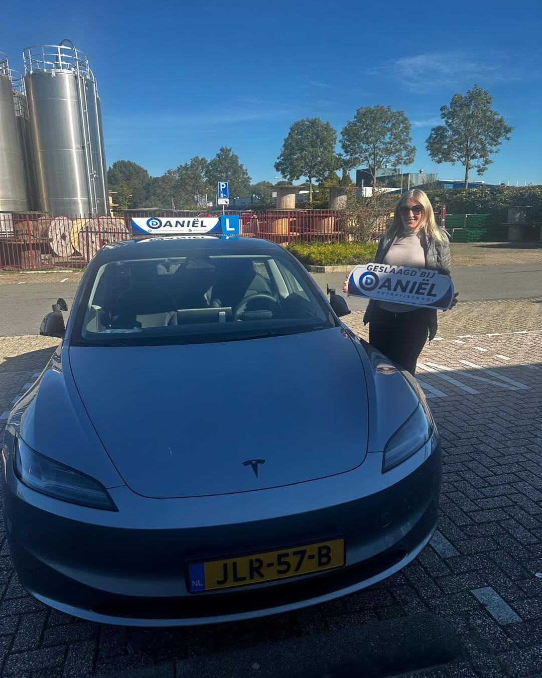Geslaagde leerling van Autorijschool Daniël met een geslaagd-bord bij de lesauto